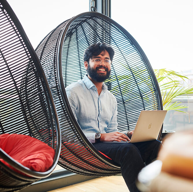 Man sat on a hanging chair with his laptop, smiling at someone